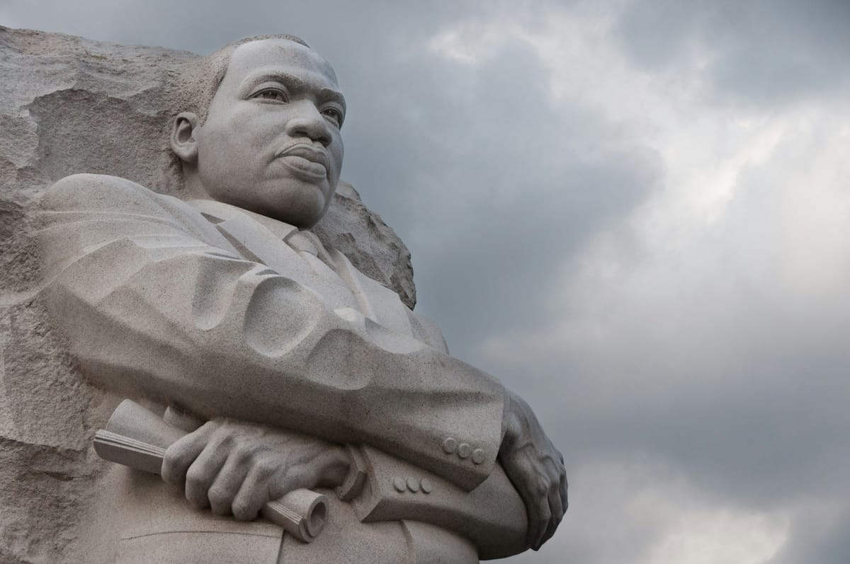 Close-up, low-angle view of the Martin Luther King Jr. Memorial sculpture, showing Dr. King carved in pale stone with arms crossed and holding a rolled document. 